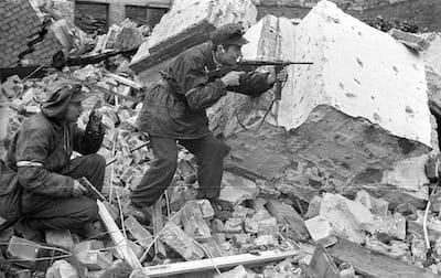 Two armed Polish soldiers fighting through the rubble of Warsaw.